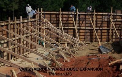 Construction site: warehouse expansion in Meridian, MS, with workers, wooden frames, and supports.