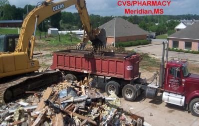 Demolition of CVS Pharmacy in Meridian, MS. Excavator loading debris into a red dump truck.