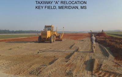 Taxiway construction at Key Field in Meridian, MS. A yellow grader and worker stand on the dirt runway.