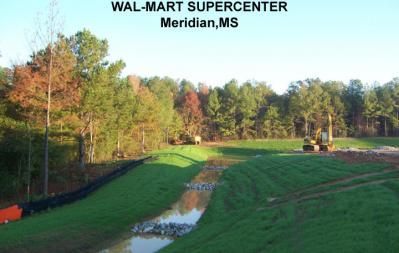 Construction site for a Wal-Mart Supercenter in Meridian, MS, with a grassy drainage channel and construction equipment.