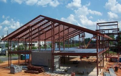 Steel frame construction of a building, brown girders and beams, on a construction site under a blue sky.