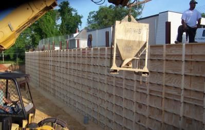 Construction site with crane lifting concrete hopper to pour concrete into a wooden formwork for a wall.