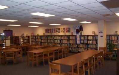 School library interior with bookshelves, tables, and chairs.