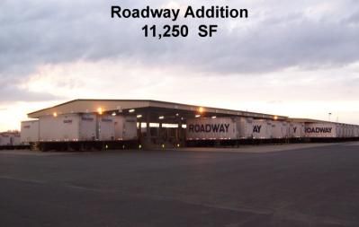 Roadway facility with multiple trailers loading/unloading under a covered area; overcast sky.