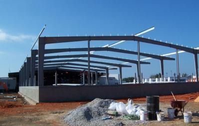 Steel frame of a building under construction, on a concrete foundation, against a blue sky.