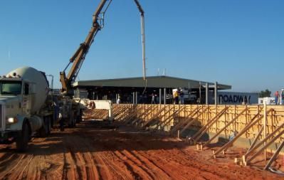 Concrete truck pouring concrete into wooden forms at a construction site, building a structure.