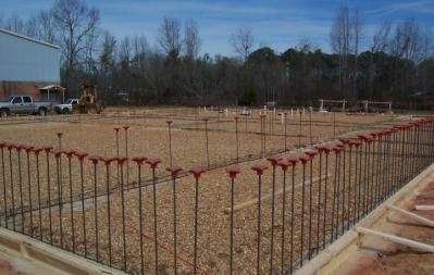 Construction site with foundation formwork, rebar, and grading; a light blue sky.