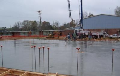 Construction site with freshly poured concrete; workers and a pump truck are visible near a building.