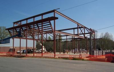 Steel frame of a building under construction, with orange safety fencing around the perimeter.