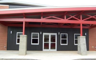Entrance to a building with black siding, red canopy, and white-framed windows and doors.
