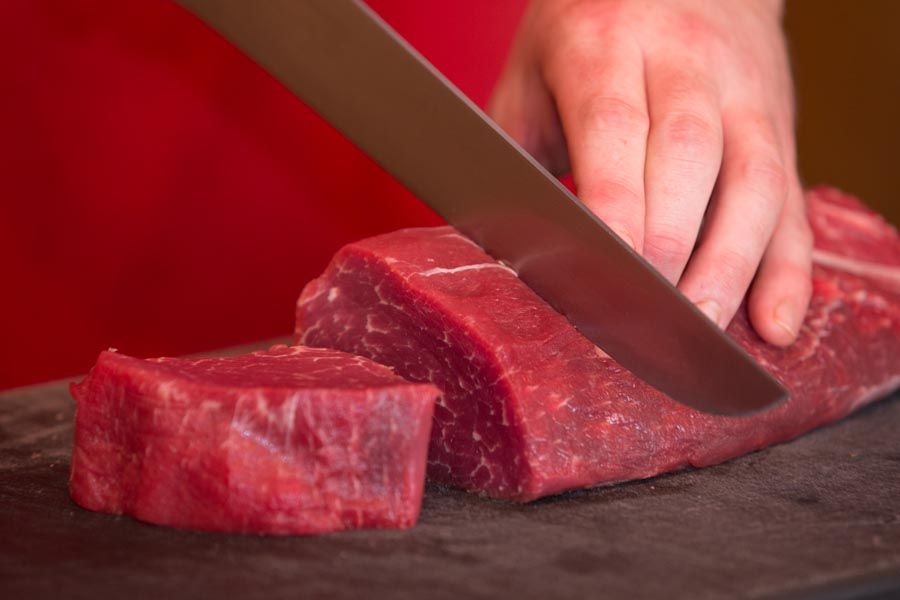 Rohes Rindfleisch mit einem großen Messer auf einem Schneidebrett von Hand schneiden