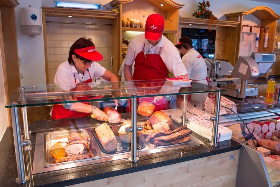 Menschen hinter der Theke einer Bäckerei bereiten Gebäck in einer Glasvitrine zu.