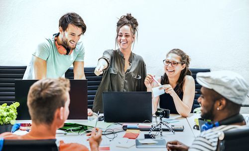 Um grupo de pessoas está sentado ao redor de uma mesa com laptops.