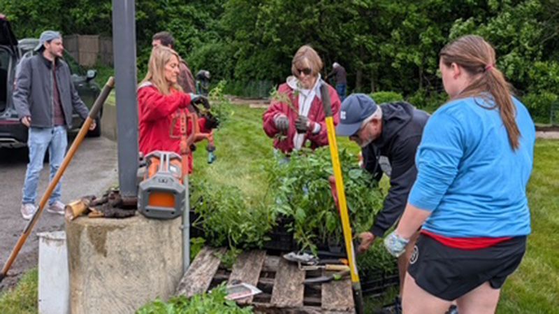 People planting flowers next to a building, with tools and a pallet.