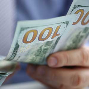 Hands counting several $100 bills. Focus on the bills, with partial view of person's hands.