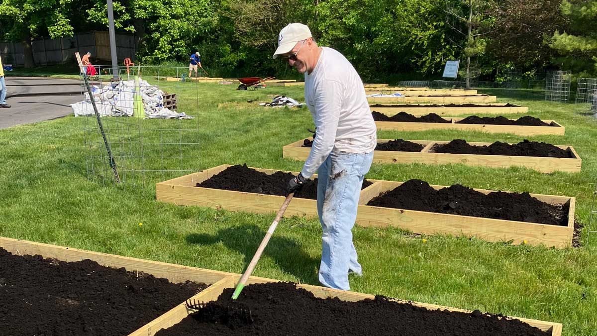 Man raking soil in raised garden beds on a sunny day.