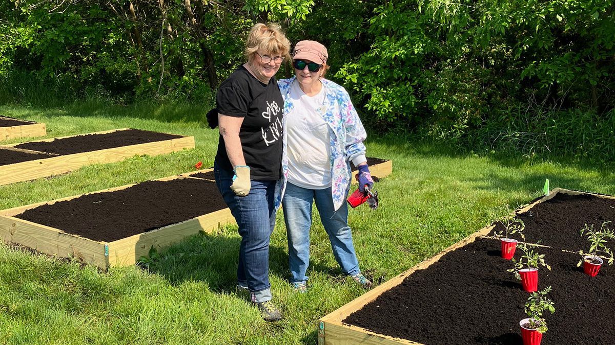 Two people smile while gardening in raised beds.