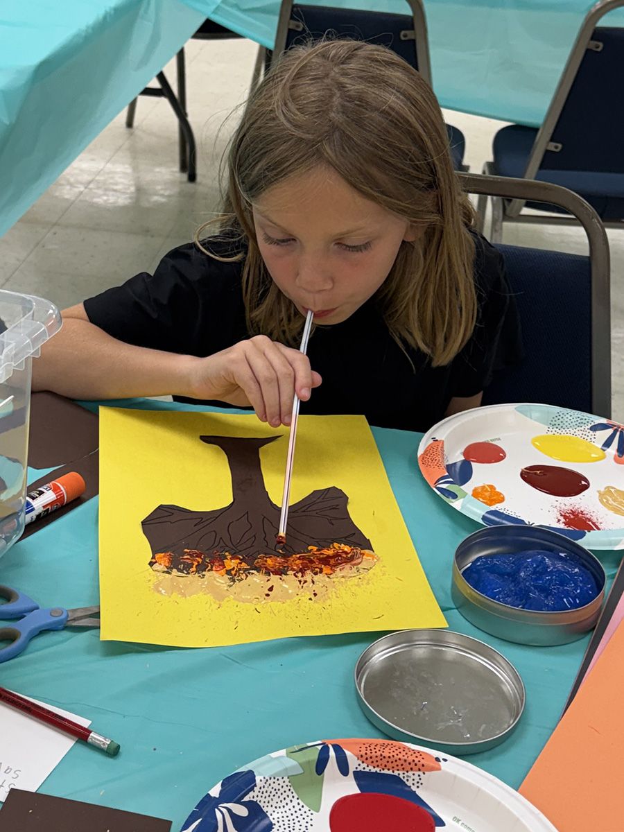 Child painting at a table with brown, orange, and blue paint on yellow paper