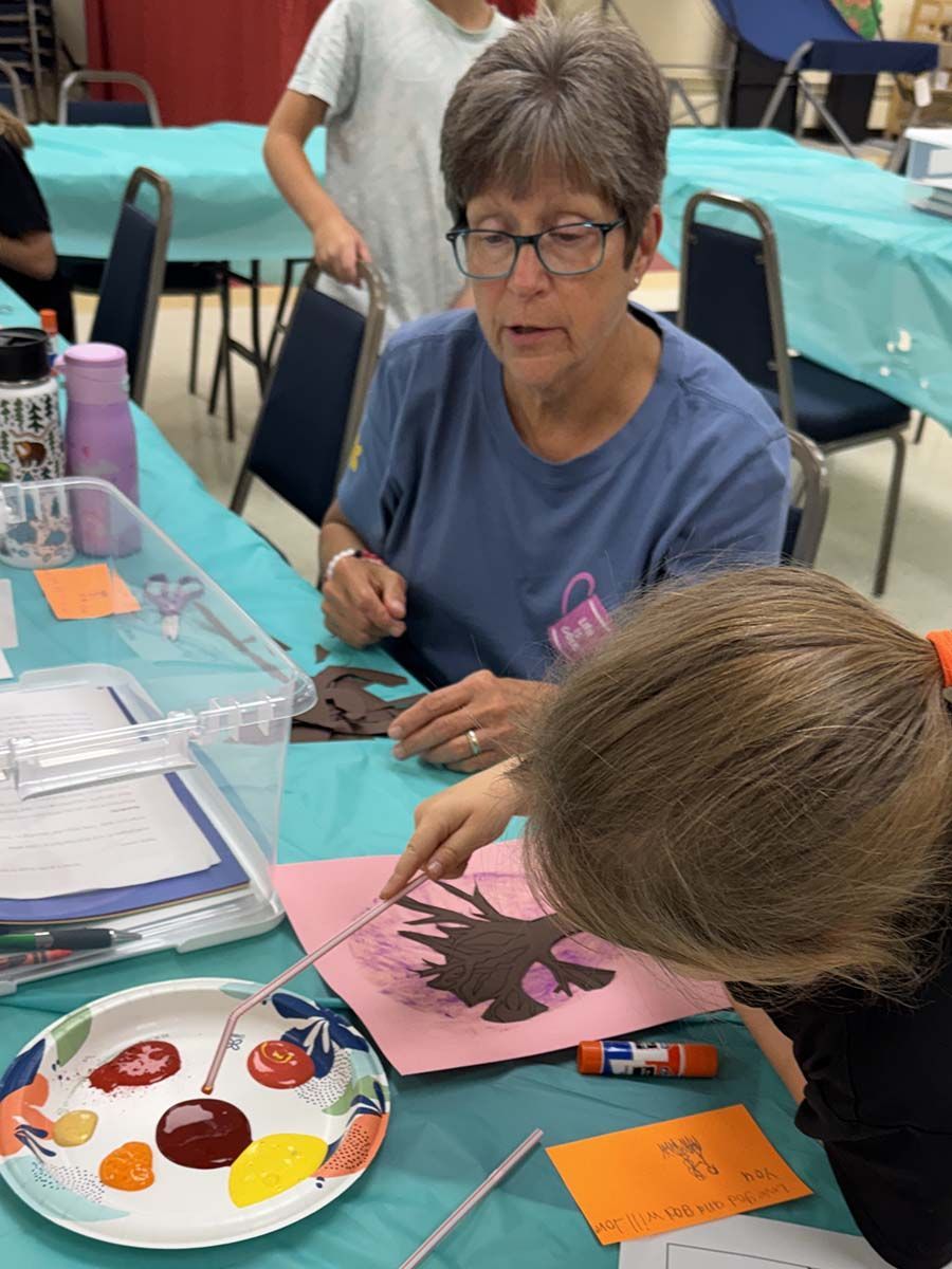 People painting at a craft table with watercolor palettes and paper in a classroom setting