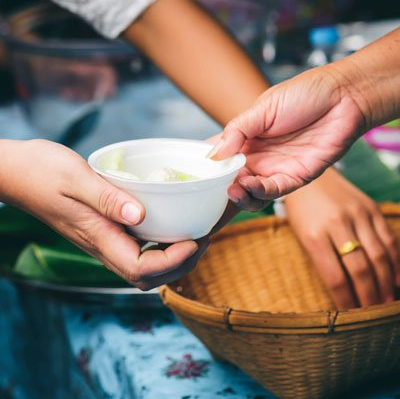 Hands holding a bowl of food, passing it to another person near a basket.