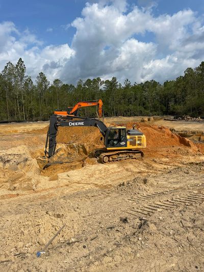 Excavator and dump truck at a dirt construction site under a cloudy sky