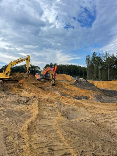 Two excavators working on a dirt construction site under a cloudy blue sky