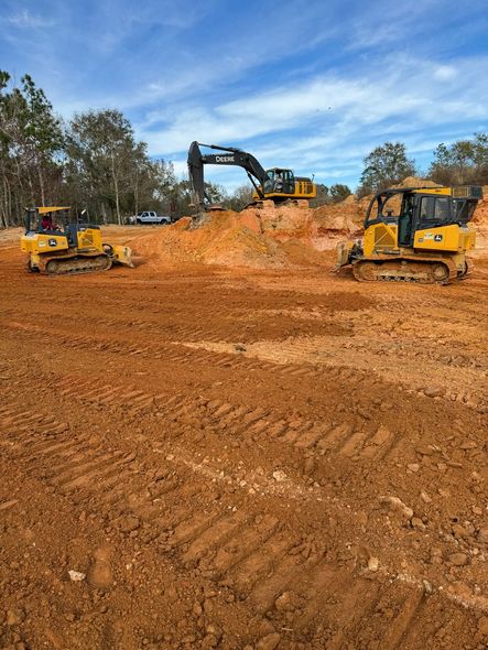 Two yellow bulldozers and an excavator working on a dirt construction site under a blue sky
