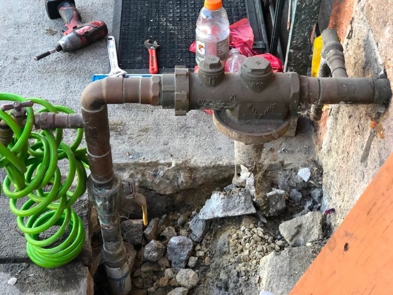 Water meter and pipes with tools, partially exposed in concrete, and a green hose.