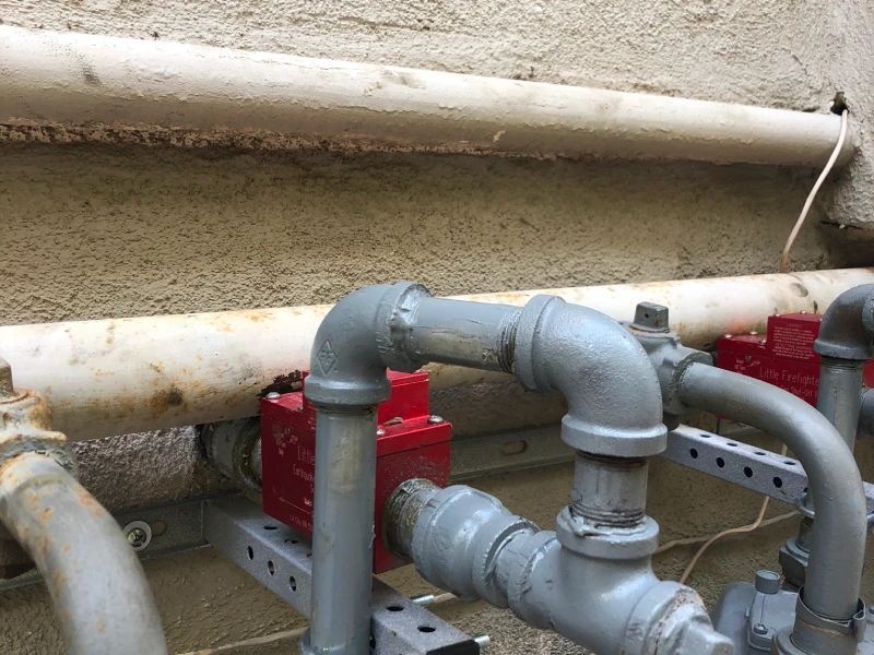 Gray pipes and red valves mounted on a concrete wall. White insulated pipe above.