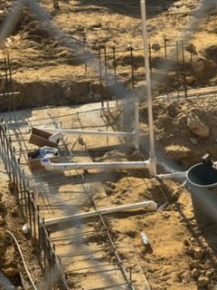 Construction foundation with rebar, concrete forms, and a bucket in a dirt excavation area