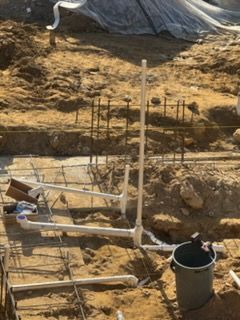 Construction site with exposed soil, metal pipes, rebar stakes, and a bucket near a trench.