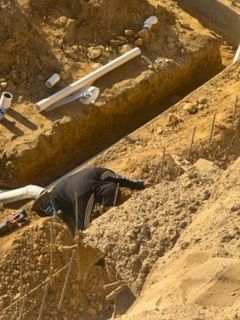 Person in dark clothing lying on a rocky dirt slope near a trench with pipes.