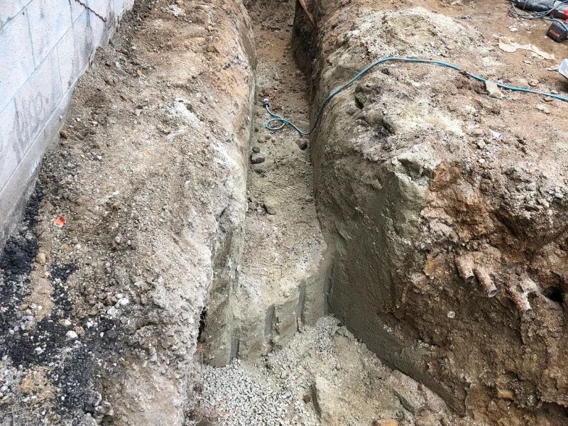 Trenches dug alongside a wall with exposed soil and small stones.