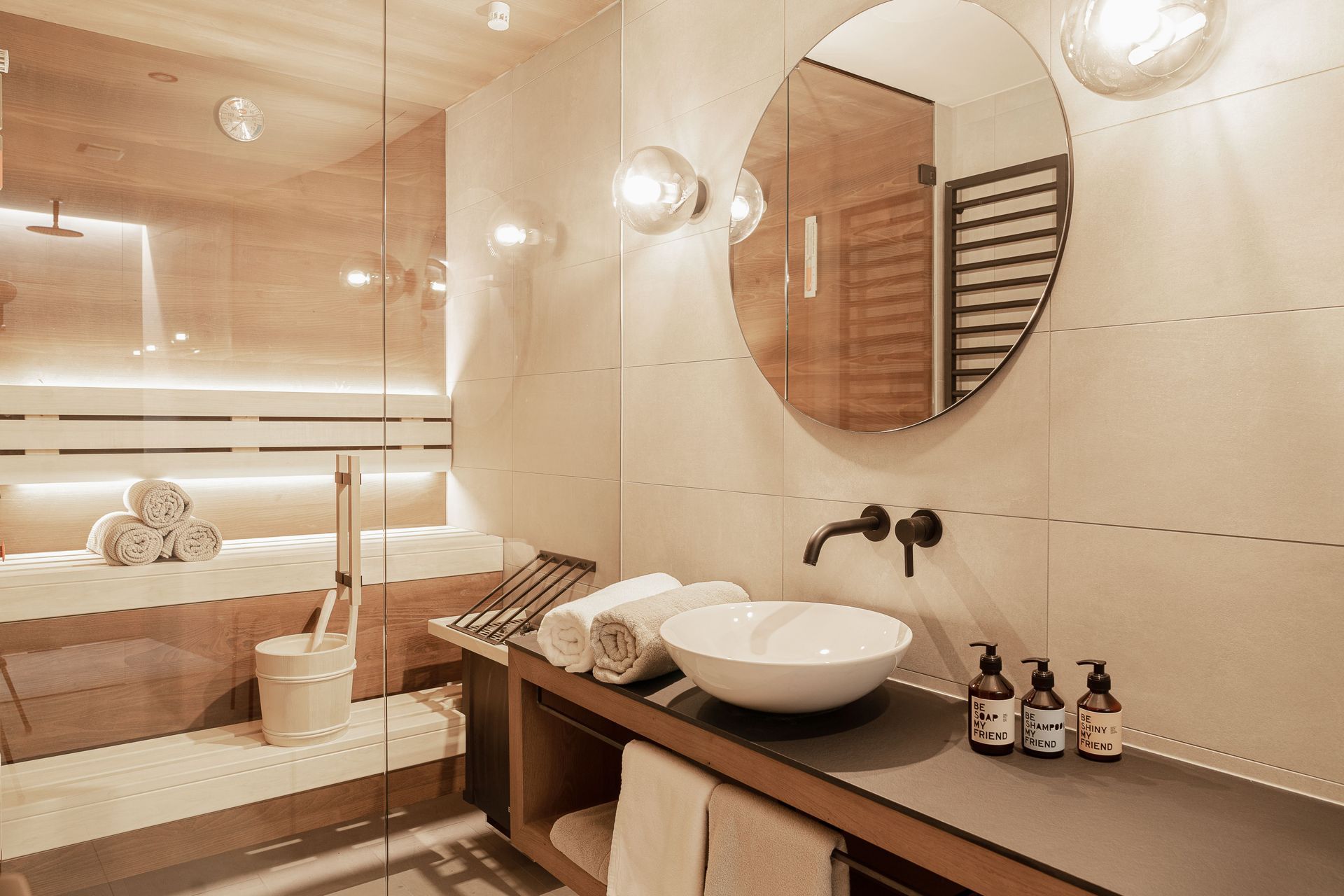 Bright modern bathroom with double vanity, large mirror, freestanding tub, and windows overlooking greenery