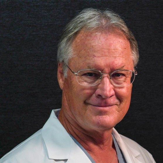 A man wearing glasses and a white lab coat smiles for the camera