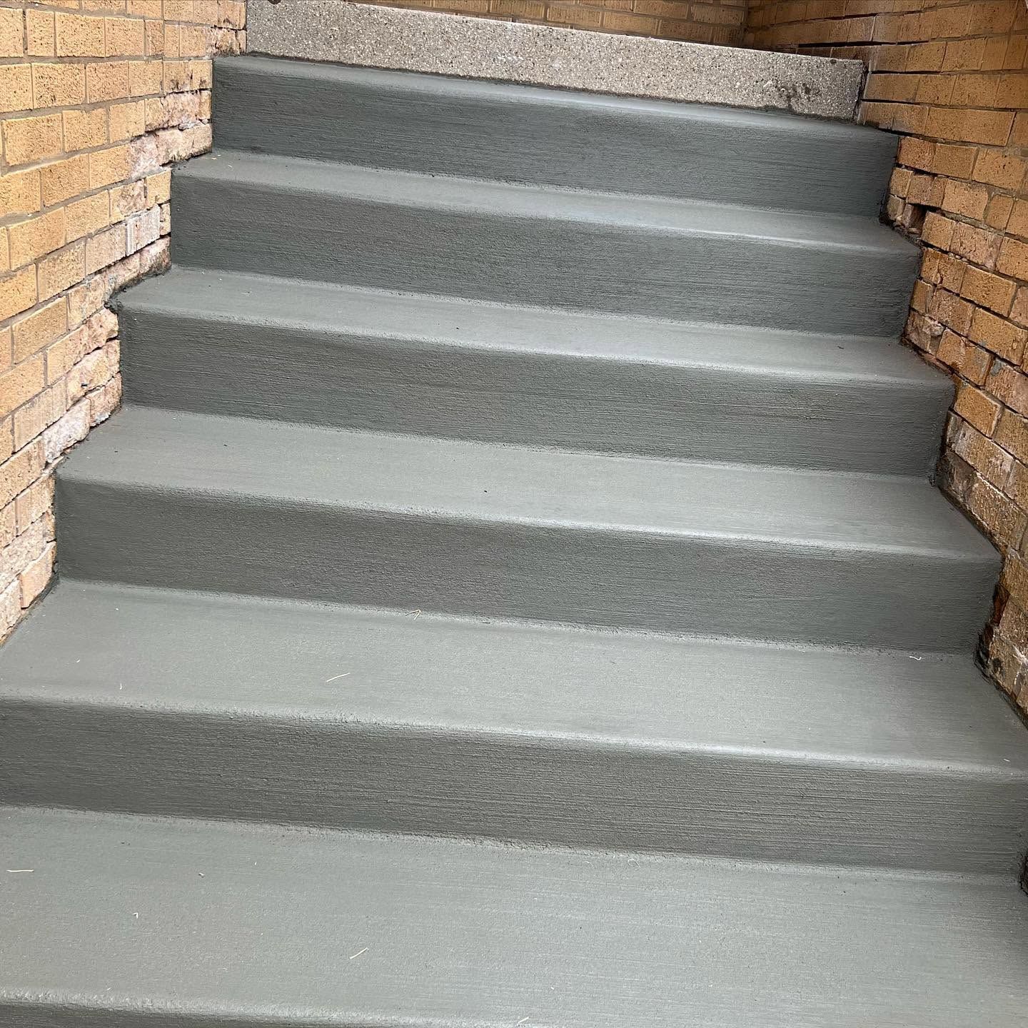 Gray concrete stairs between brick walls leading upward