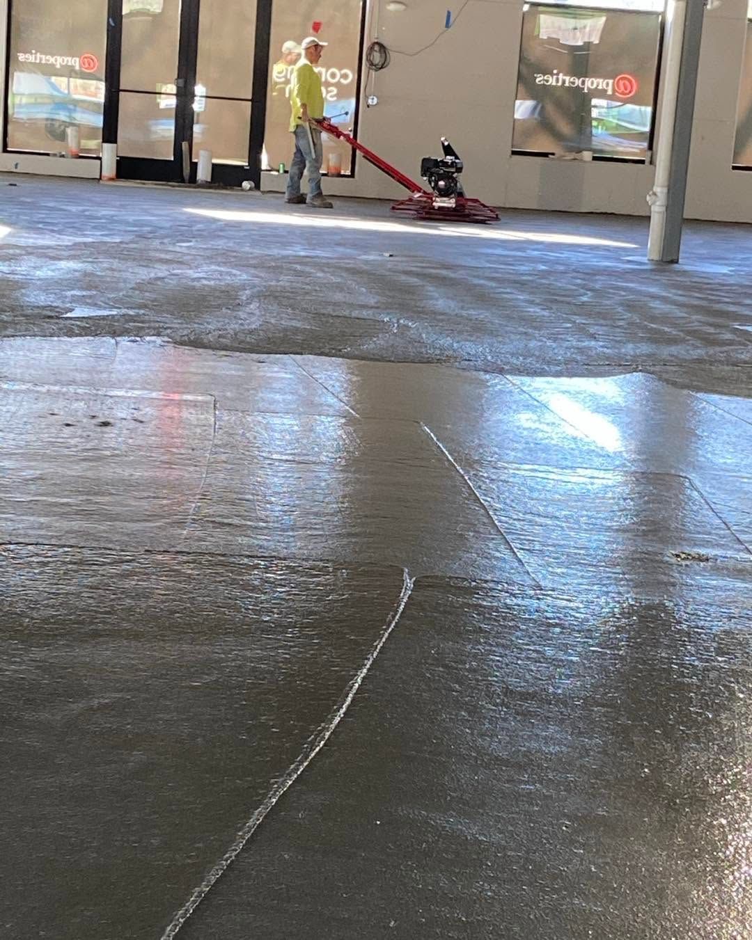 Person operating a red floor scrubber in a shiny indoor lobby with glass doors.