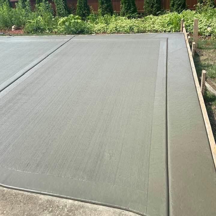 Freshly poured concrete driveway next to garden beds and a wooden fence