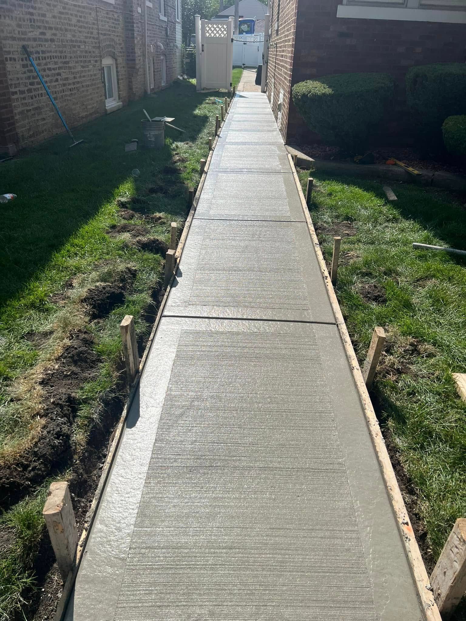 Narrow concrete walkway between brick buildings, with grass on both sides, leading to a gate.