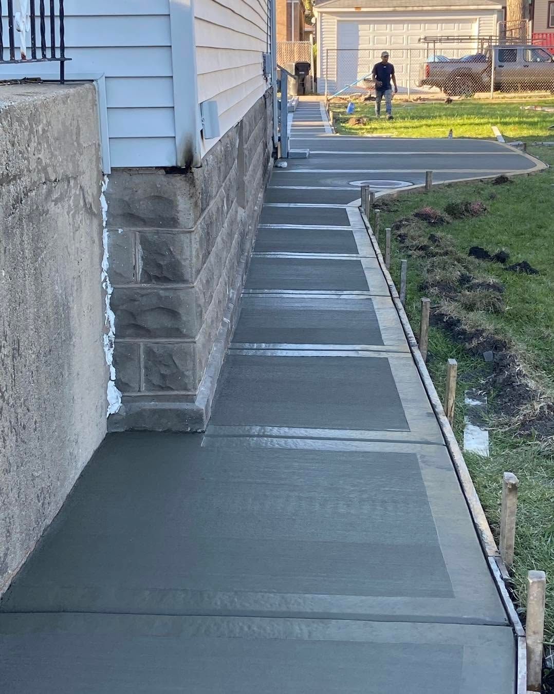 Concrete sidewalk alongside a house and stone wall, leading to a gate and yard