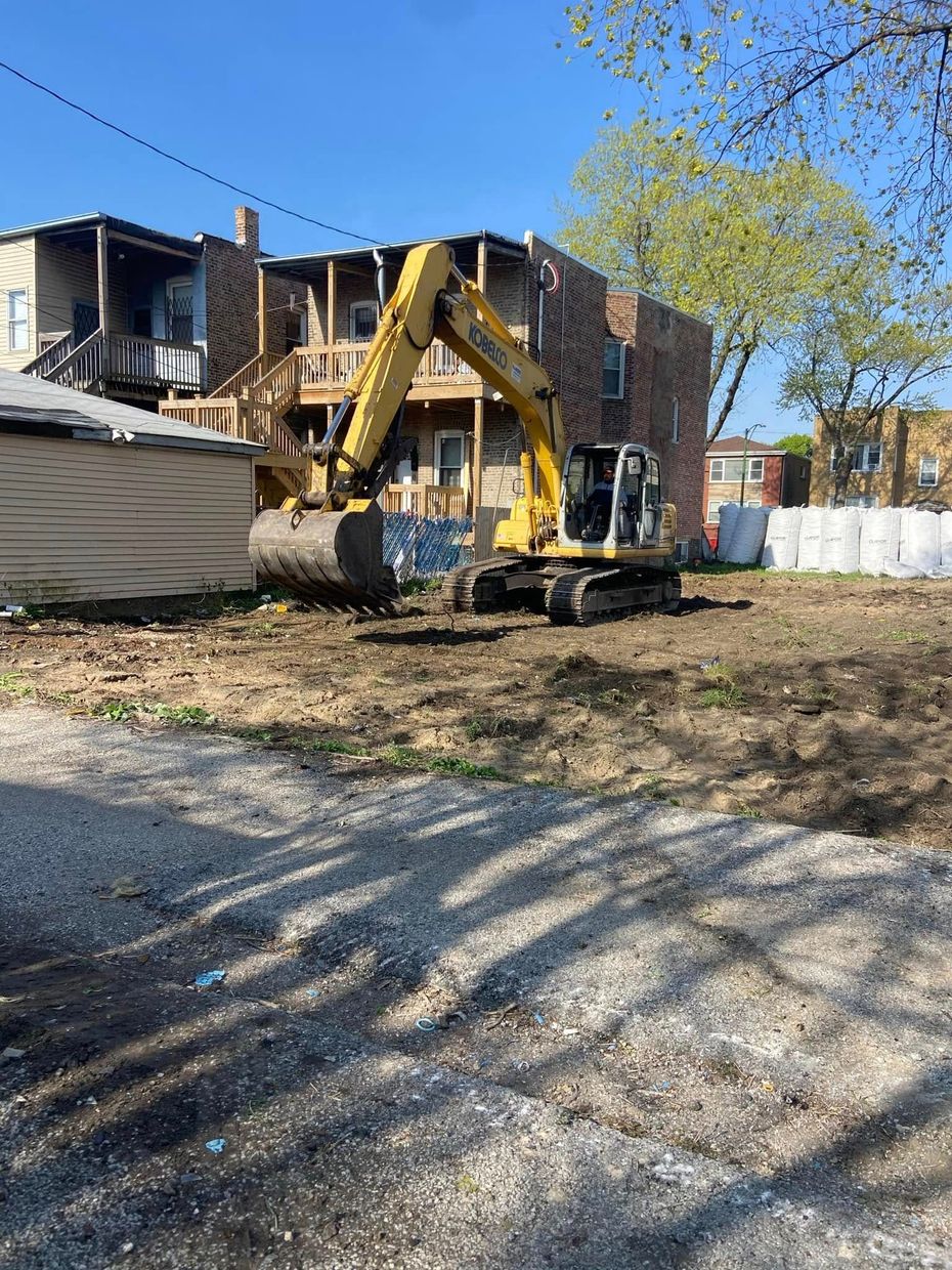 Yellow excavator demolishing a building beside a gravel lot and rubble under a blue sky