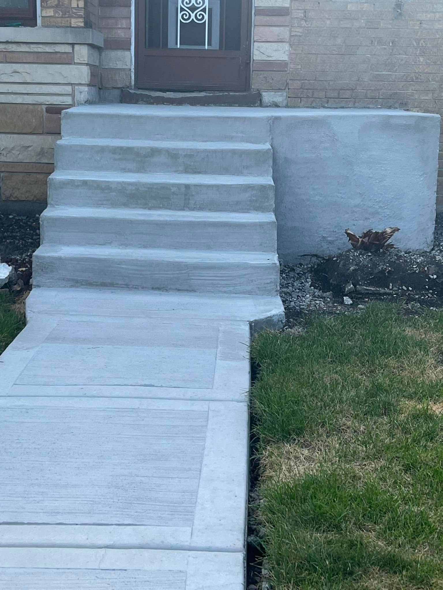 Concrete front steps leading to a house entrance beside a grass lawn and stone wall
