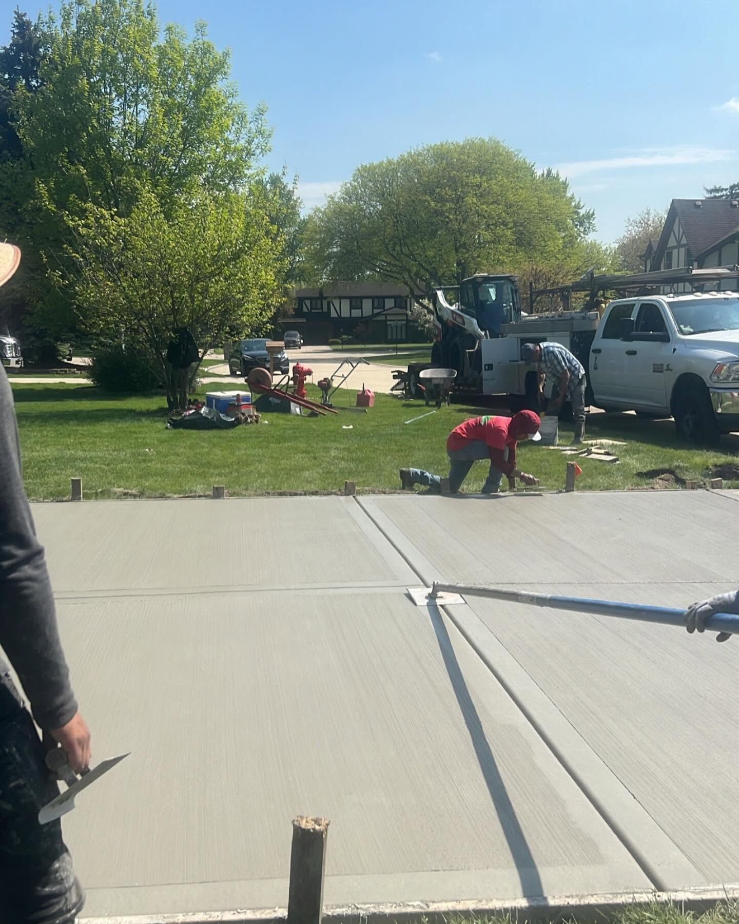Workers installing a gray patio slab in a grassy yard, with trucks and tools nearby