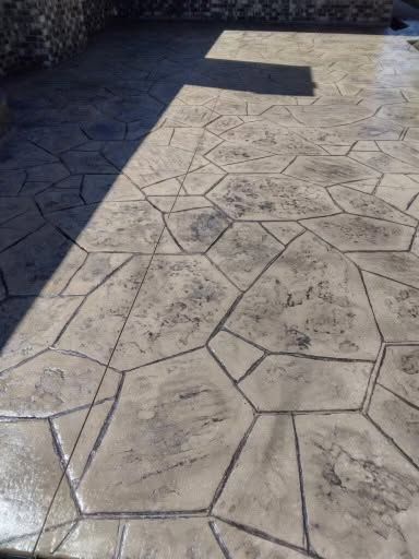 Stamped concrete patio in sunlight and shadow, with a stone wall at the top edge.