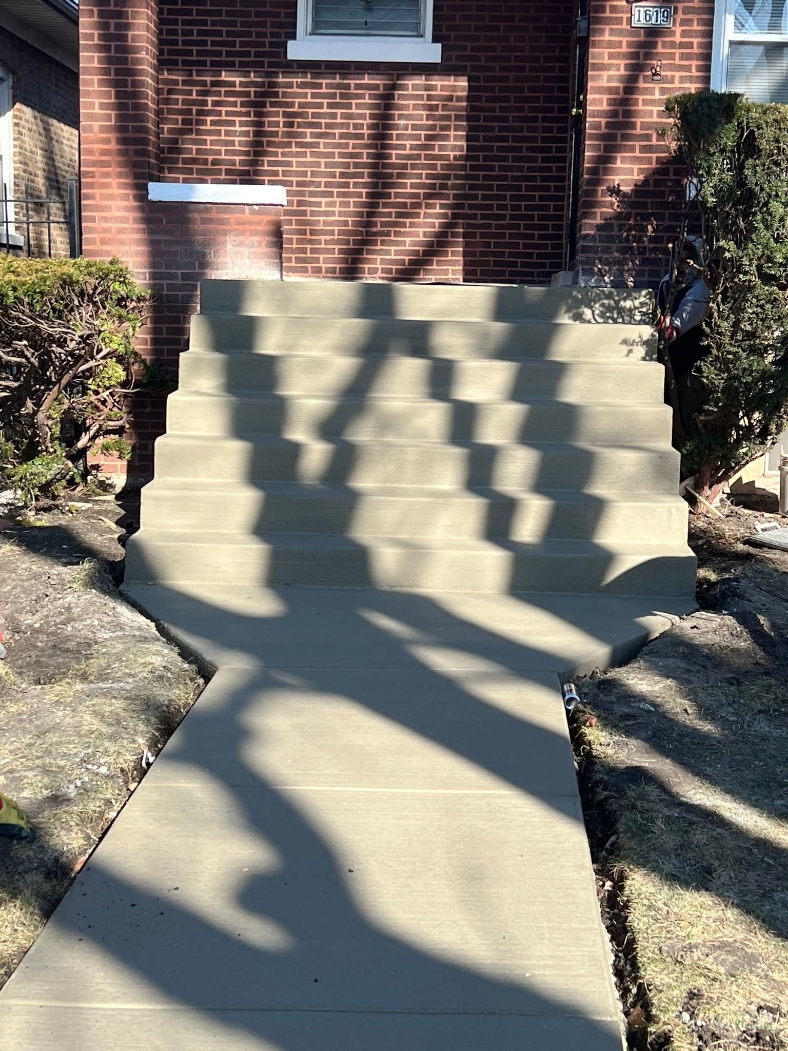 Concrete front steps with strong tree shadows leading up to a brick house entrance