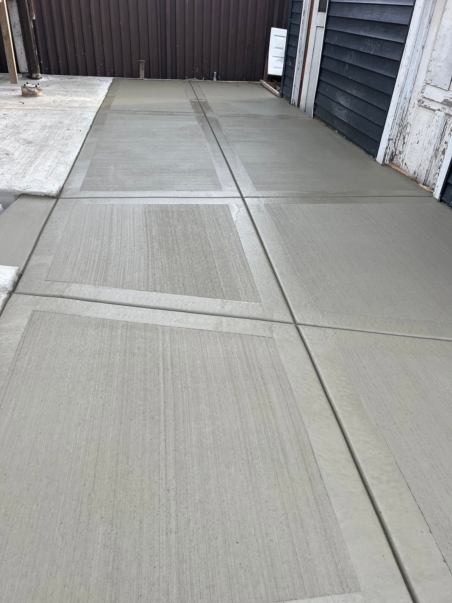 Concrete driveway/alley between garages with dark doors and a fenced end wall