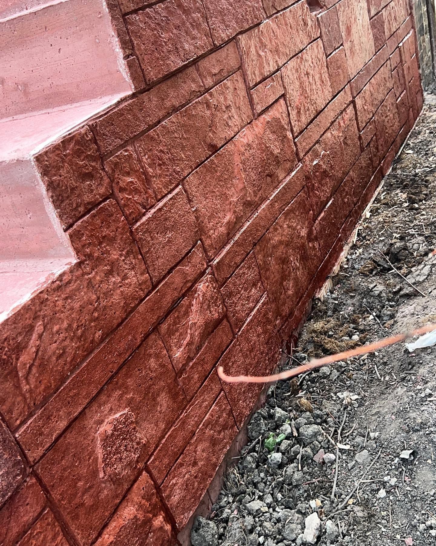 Close-up of a brick wall being painted dark red with a roller brush on the ground
