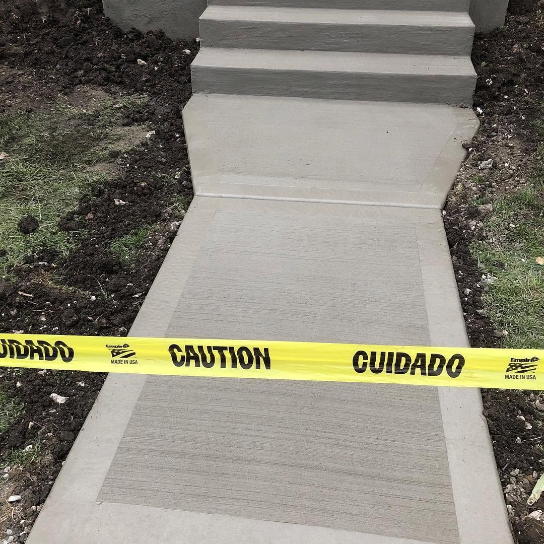 Concrete walkway blocked by yellow caution tape, with damaged steps ahead and grass on both sides