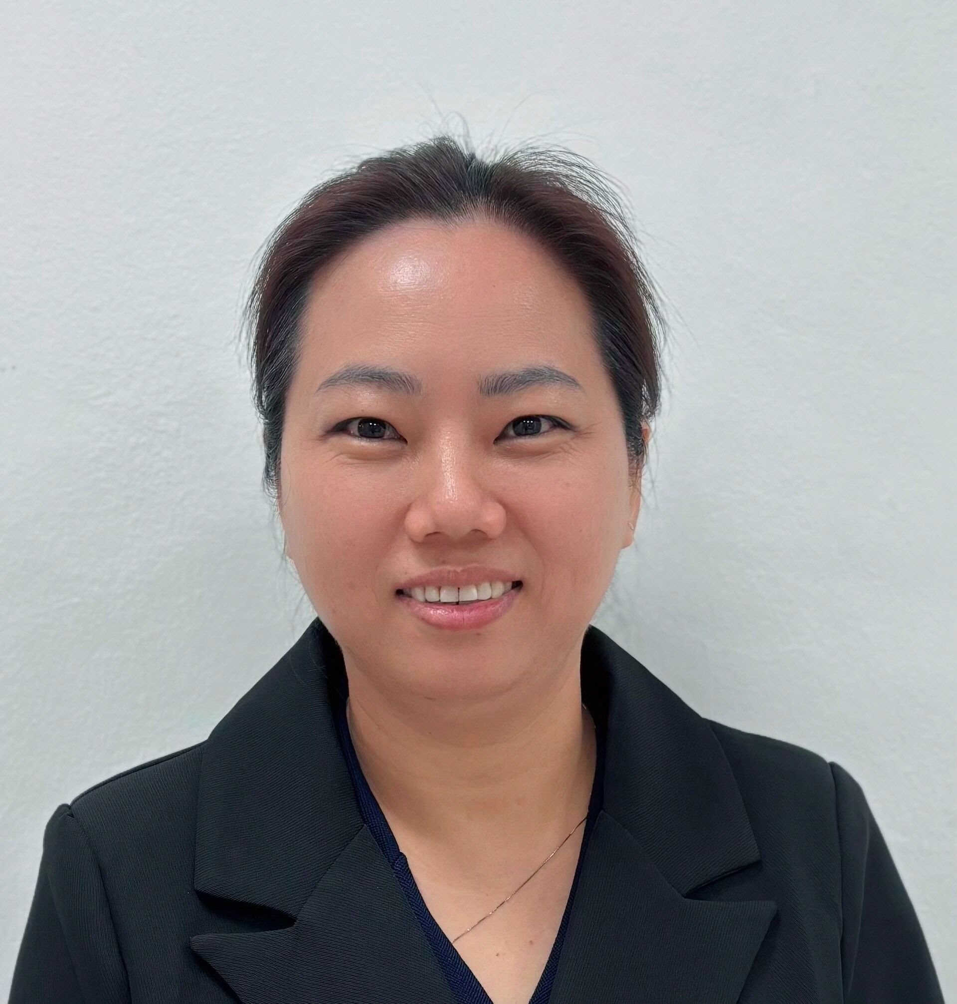 Portrait of a person in a black blazer, smiling against a plain white background