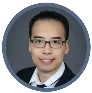 Headshot of a person wearing glasses, a dark suit, and a white shirt with a tie, on a gray background